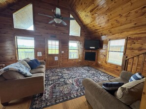 L’intérieur d’un chalet en bois, avec deux canapés, un tapis à motifs, un ventilateur de plafond et un téléviseur.