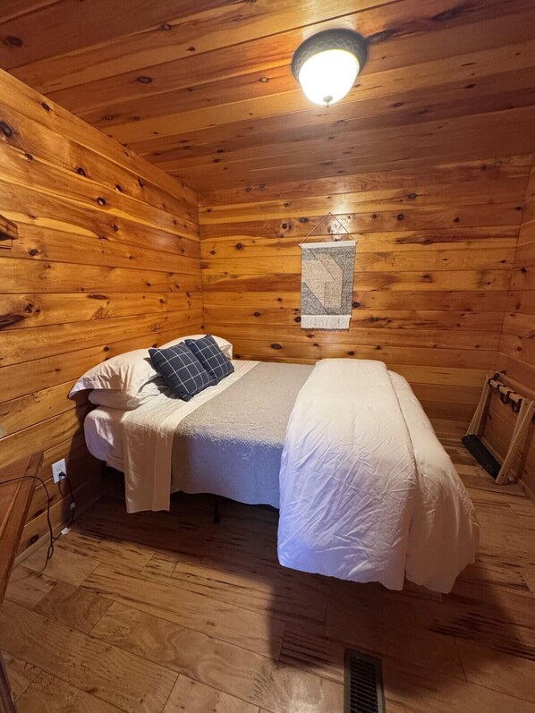 A wooden cabin room with a bed, a hanging tapestry, and a ceiling light.