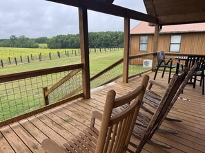 Une terrasse en bois offrant une vue sur un champ clôturé, un espace couvert avec des chaises et un bâtiment doté de fenêtres.
