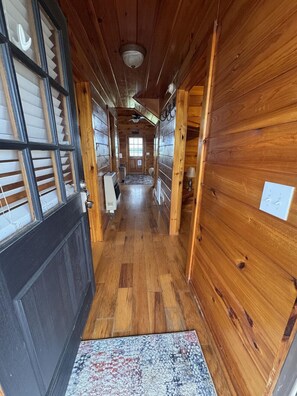 A wooden hallway with a rug, a ceiling fan, and a door at the end.