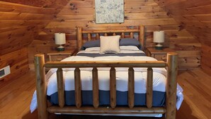 Una habitación con paneles de madera, una cama, dos mesitas de noche, un ventilador de techo y un cuadro en la pared.