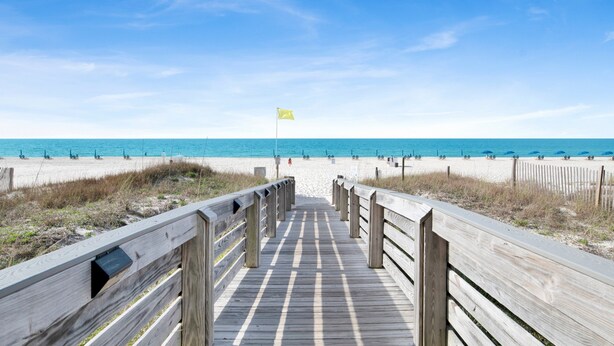 A wooden boardwalk leading to a beach with a flag. - Beachfront 2BR @ Admiral Quarters • Sleeps 8 • Stunning Views (Orange Beach)