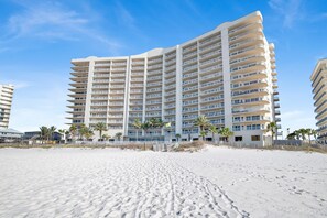 Ein Strandhotel mit mehreren Balkonen, Palmen und einem Sandstrand.
