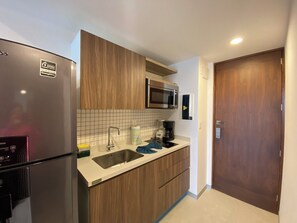 A compact kitchen with a built-in microwave, a stainless steel sink, and a refrigerator. - Chic studio in the best location. Swimming pool and gym. (Playa del Carmen)