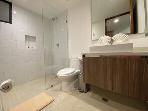 A modern bathroom with a glass shower enclosure, a toilet, a sink with a wooden vanity, and a mirror above the sink. - Chic studio in the best location. Swimming pool and gym. (Playa del Carmen)