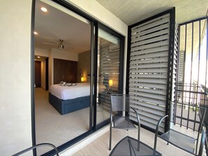 A modern bedroom with a bed, a chair, and a balcony with metal railings. - Chic studio in the best location. Swimming pool and gym. (Playa del Carmen)