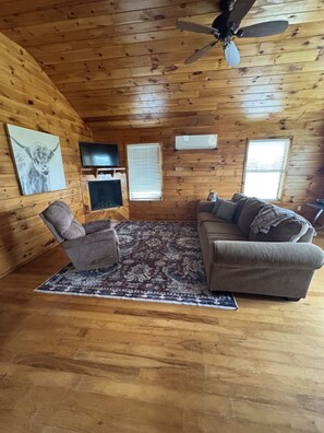 A log cabin interior with a ceiling fan, a television, a fireplace, and a couch.