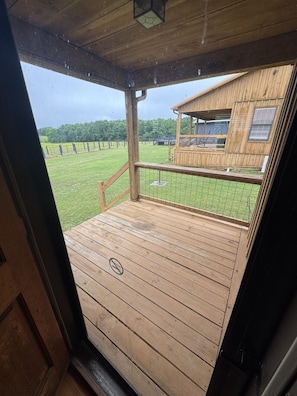 A wooden deck with a railing, a view of a fenced property, and a building with windows.