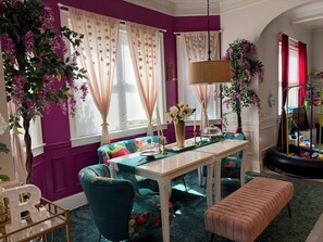 Ein Zimmer mit einer violetten Wand, einem floralen Sofa, einem Tisch mit einer Vase und einer Bank.