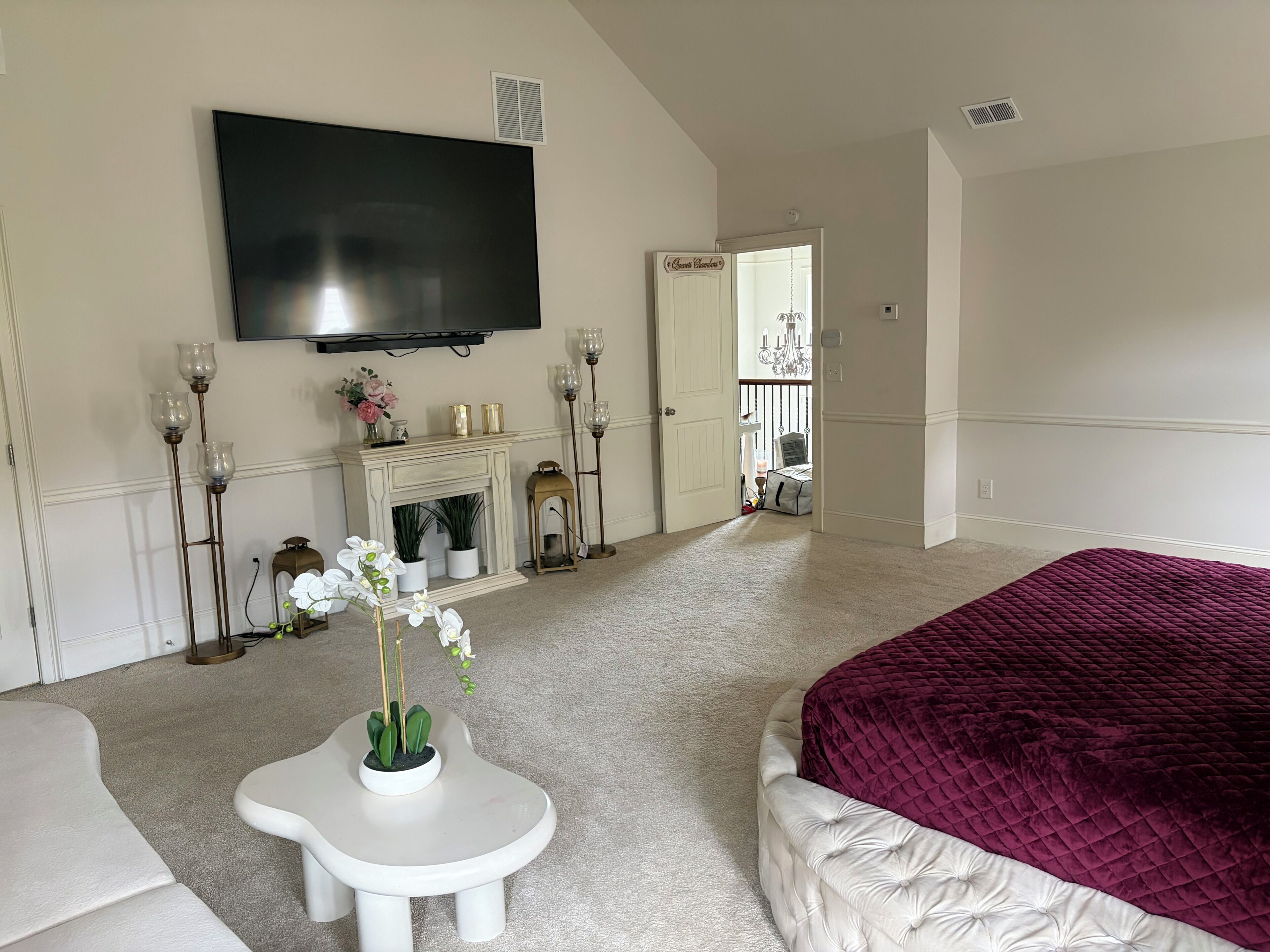 A bedroom with a large bed, a flat-screen TV mounted on the wall, a fireplace, and a door leading to a balcony.