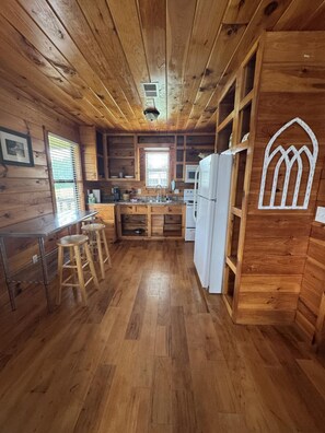 Ein Holzblockhaus-Innenraum mit Küche, Bar und einem Esstisch mit Hockern.