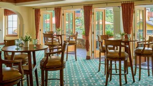 Un comedor con mesas y sillas de madera, ventanas amplias con cortinas y vistas a zonas verdes.