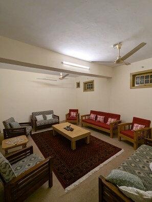 A living room with a sofa set, a coffee table, a patterned rug, and ceiling fans.