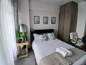 Ein Hotelzimmer mit einem Bett, einem Sessel, einem Schreibtisch mit Spiegel und einem Kleiderschrank.