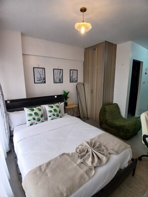 A neatly made bed with a decorative pillow, a green chair, and a wooden wardrobe in a hotel room. - Elegant Studio Apartment for Business & Leisure (Nairobi)