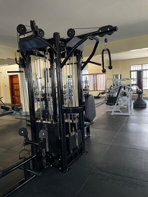 Ein Fitnessstudio mit verschiedenen Trainingsgeräten, darunter ein Kabelzuggerät und eine Langhantelbank.