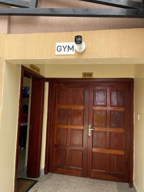 Eine doppelte Holztür, über ihr ein Schild mit der Aufschrift 'GYM', links ein Empfangsschild und darüber ein Schild mit 'RECEPTION'.