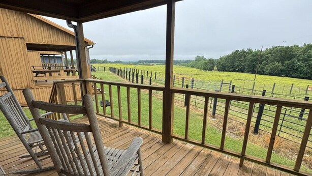 Une terrasse en bois offrant une vue sur un champ clôturé et un bâtiment situé au loin.