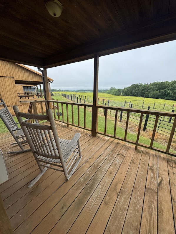 A wooden deck with a view of a fenced field and a building in the background.