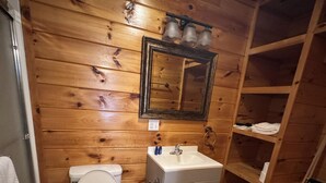 Une salle de bain aux murs lambrissés, équipée de toilettes, d’un lavabo et d’un miroir.