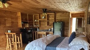 A log cabin interior with a bed, sofa, wooden dining table, kitchen area, and a ceiling fan. - Ranch House 6 at Lamb Ranch (Michie)