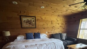 A wooden cabin bedroom with a bed, a sofa, a small table, and a ceiling fan. - Ranch House 6 at Lamb Ranch (Michie)