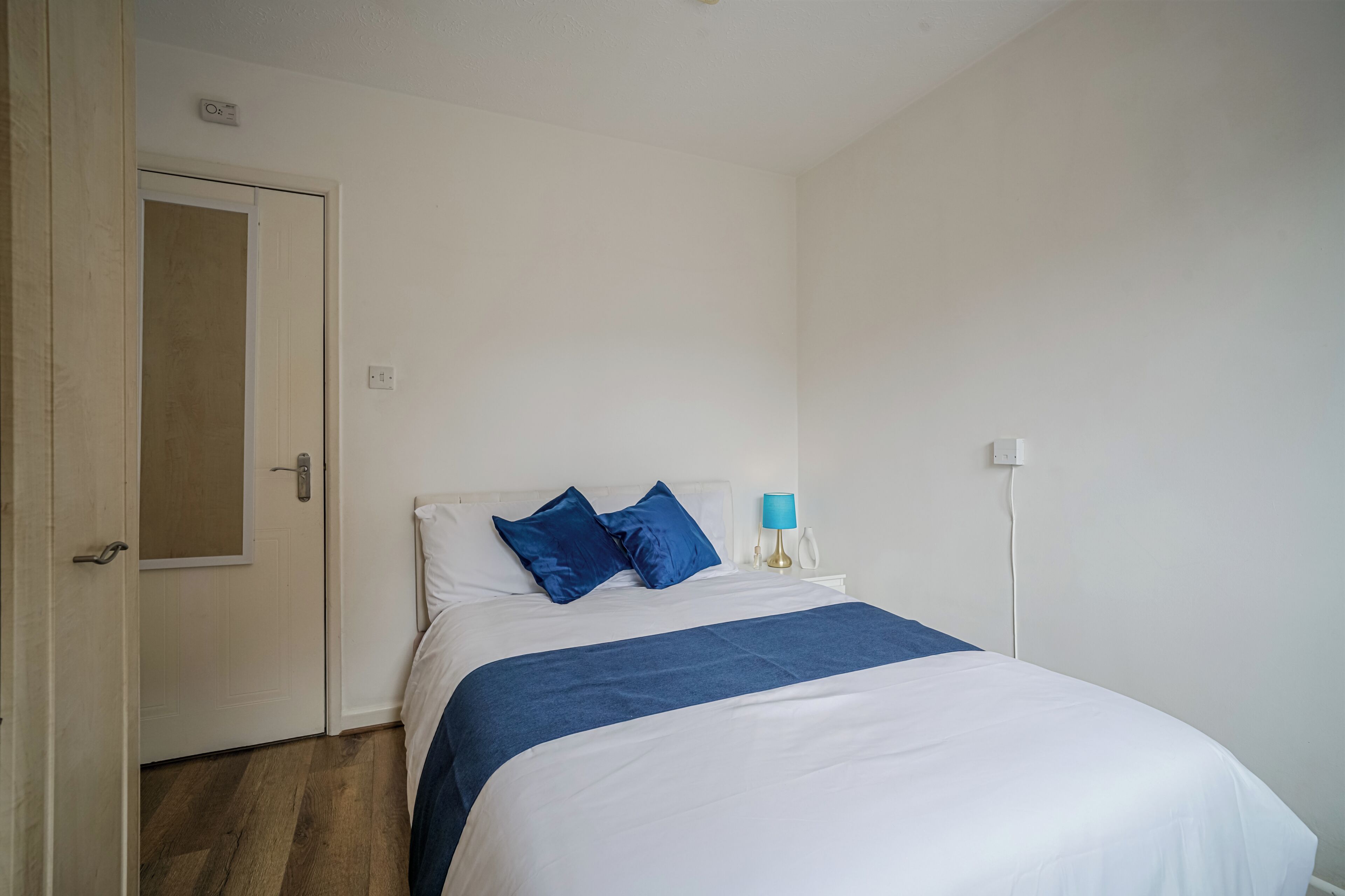 A bedroom with a bed, a nightstand, a lamp, and a door.