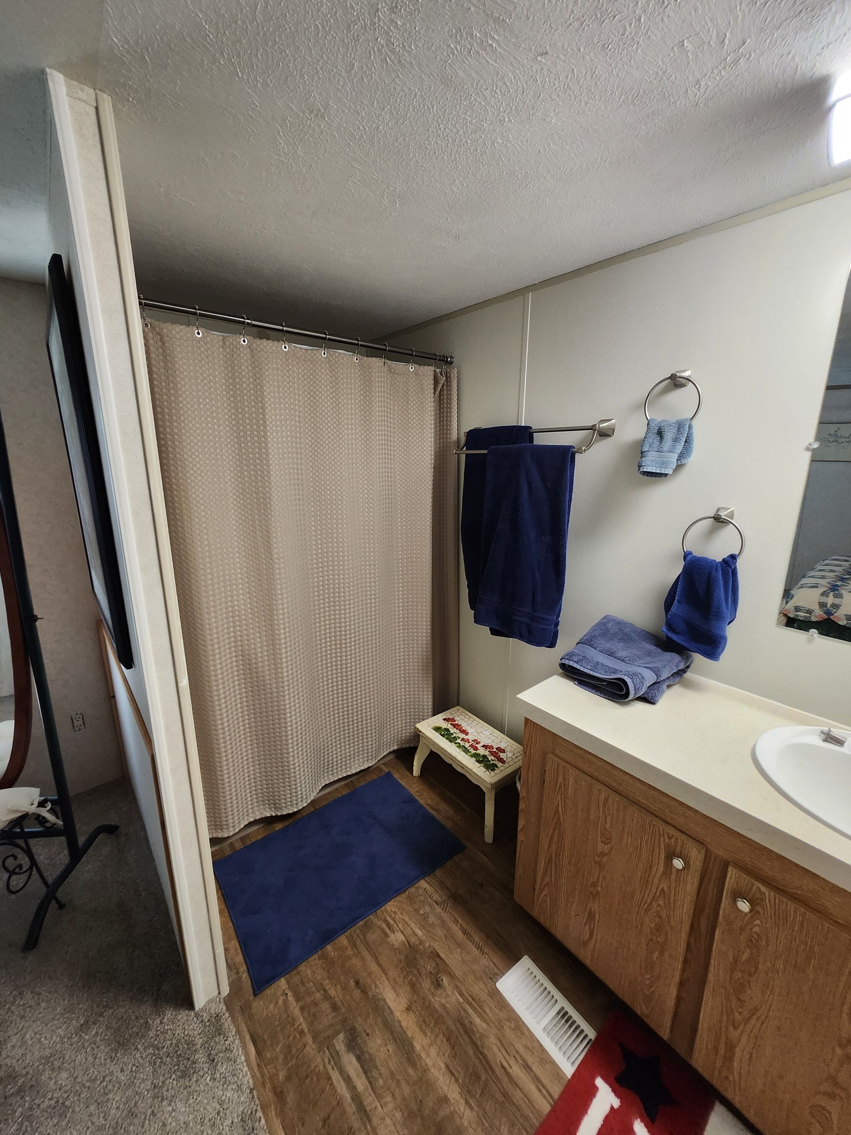 A bathroom with a shower curtain, a small step stool, a sink, and a mirror.