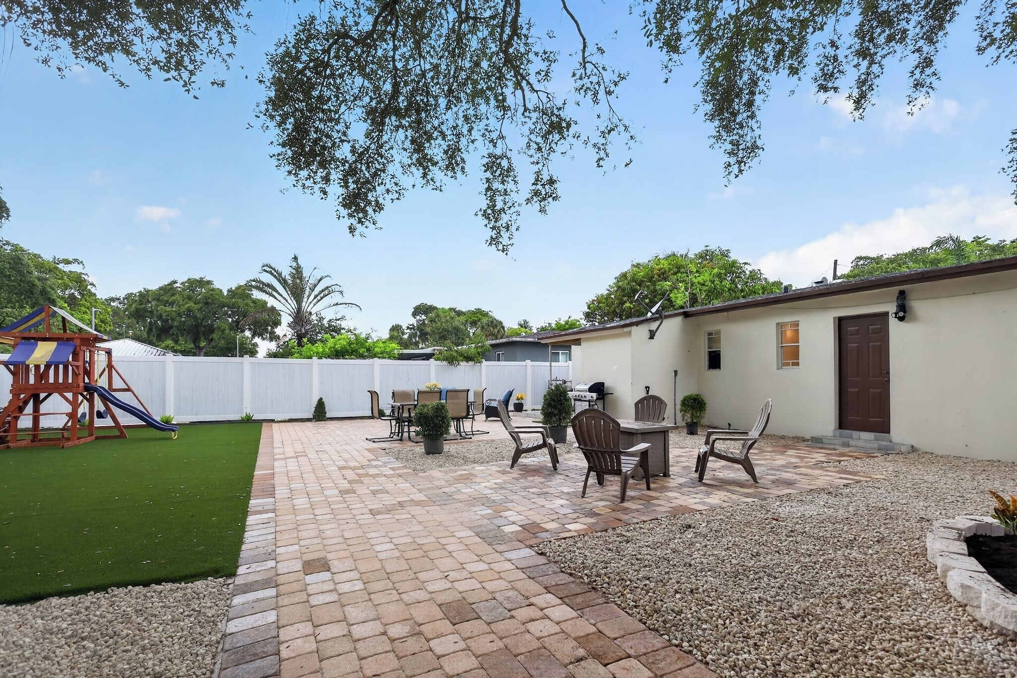 Un patio con área de juegos, mobiliario exterior y un edificio blanco.