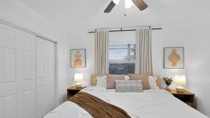 A bedroom with a bed, two bedside tables with lamps, a window with curtains, a ceiling fan, and a door. - Family Getaway • Huge Yard • Near Beach• 3BR (Hallandale Beach)