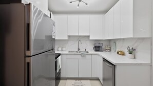 A modern kitchen with white cabinets, a stainless steel refrigerator, a built-in oven, a sink, and a ceiling light fixture. - Family Getaway • Huge Yard • Near Beach• 3BR (Hallandale Beach)