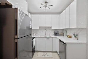 Una cocina moderna con armarios blancos, un refrigerador de acero inoxidable, horno empotrado, un lavamanos y una lámpara en el techo.