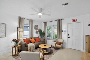 Una sala de estar moderna con ventilador de techo, un sofá, una mesa redonda y un sillón.