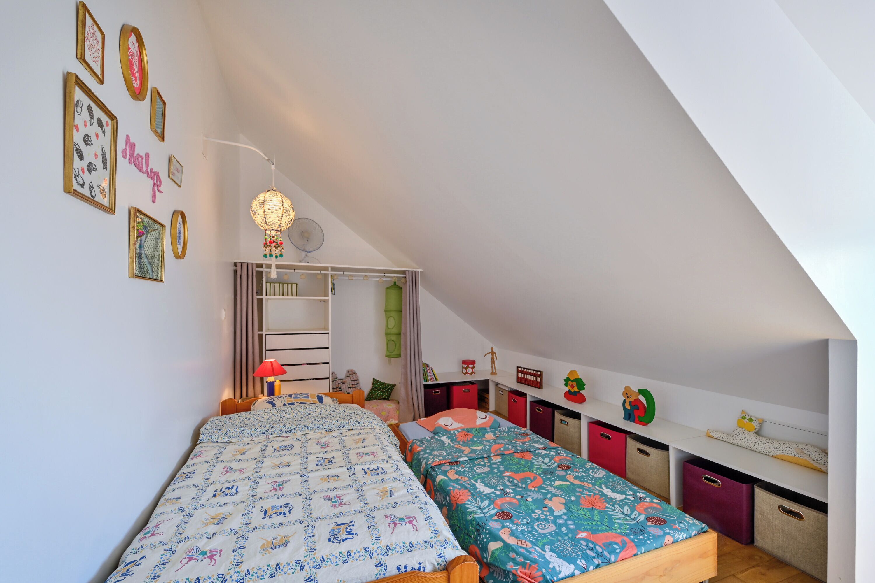 Un dormitorio con dos camas, un escritorio y una estantería llena de juguetes.