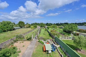 A fenced outdoor area with a table and chairs, a pathway, and a view of a lake. - Le Roseau - Véranda et Jardin - Wifi (Saint-Malo-de-Guersac)