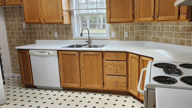 Una cocina con armarios de madera, encimera blanca, lavavajillas y estufa.