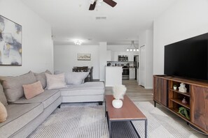 Ein modernes Wohnzimmer mit einer Couch, einem Couchtisch, einem Fernseher und einer Küche im Hintergrund.