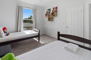 Ein Zimmer mit zwei Betten, einem Vorhangfenster, einer Tür und Wandregalen mit Charakterfiguren.