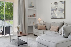 Ein Wohnzimmer mit grauem Sofa, einem kleinen Tisch, einer Lampe und einer Wand mit einem Gemälde.