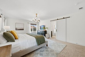 A bedroom with a bed, a chandelier, a dresser, a plant, and a door. - Old Town North Retreat Bikes, Brews & Trails (Fort Collins)