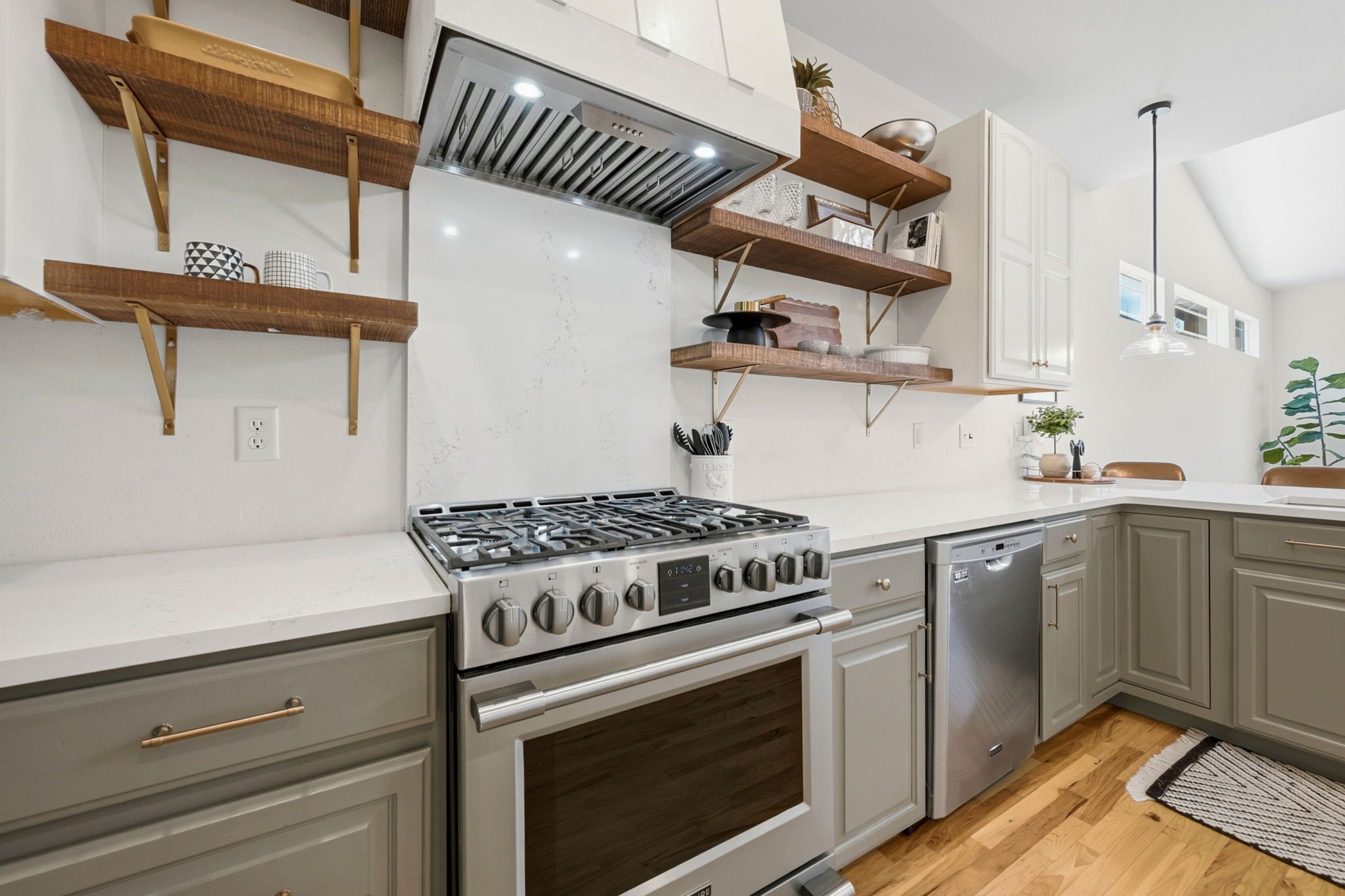 A kitchen with a gas stove, oven, dishwasher, wooden shelves, and white cabinets.
