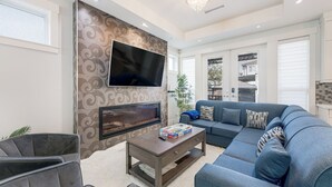 Een moderne woonkamer met een flatscreen televisie, een open haard, een hoekbank en een salontafel.