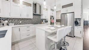 Een moderne keuken met witte kastjes, een centraal eiland met een bar en zitplaatsen, een roestvrijstalen koelkast en een magnetron.