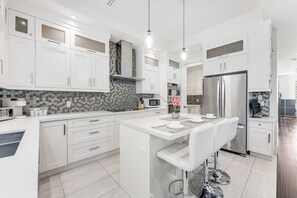 A modern kitchen with white cabinetry, a central island with bar seating, a stainless steel refrigerator, and a microwave.