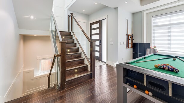 Een modern interieur met een houten trap, een pooltafel en uitzicht op de verdieping erboven.