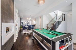 Un interior moderno con mesa de billar, escalera y zona de comedor.