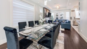 Een moderne eethoek met een glazen tafel, zwarte fauteuils en een blauwe bank op de achtergrond.