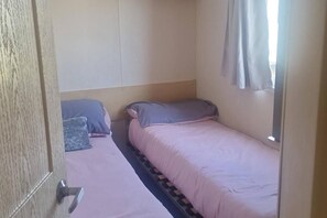 Una habitación con dos camas, una puerta de madera y un ventanal con cortinas.
