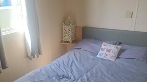 Una camera da letto con un letto, un comodino, una lampada a parete e una finestra con tende.