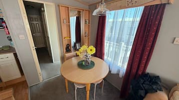 Um espaço de estar compacto com uma mesa de jantar redonda de madeira, uma kitchenette, um sofá e uma janela com cortinas.